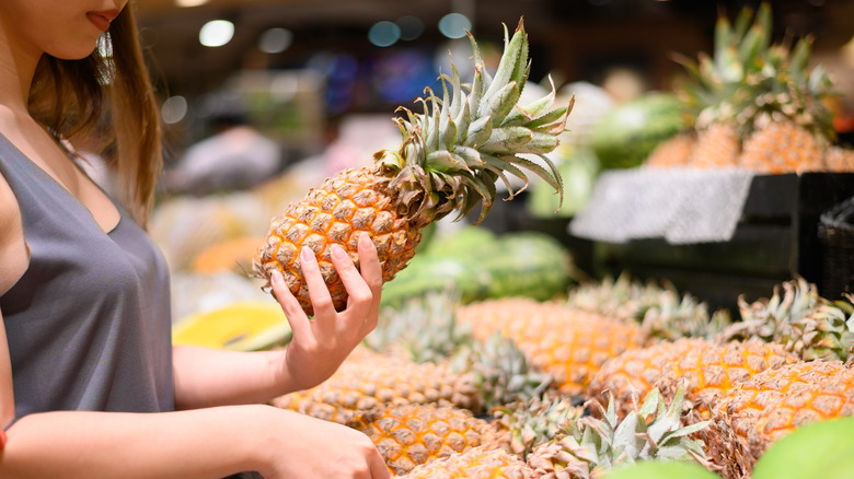 Woman choosing pineapple at store