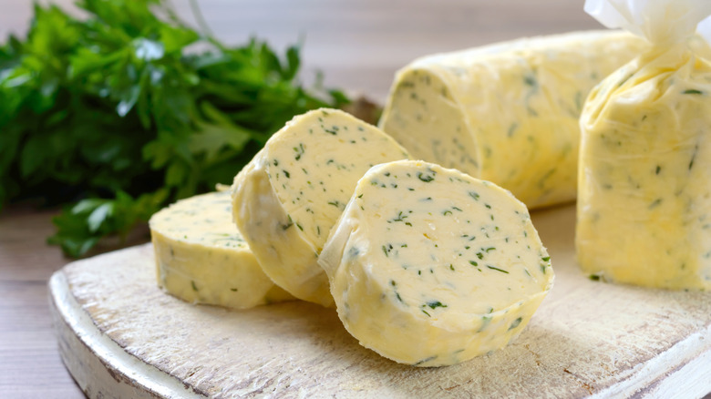 Cylinders of herb compound butter on a board with fresh herbs in background