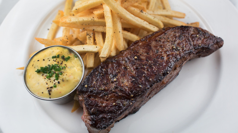 Steak frites on a plate with a pot of béarnaise sauce