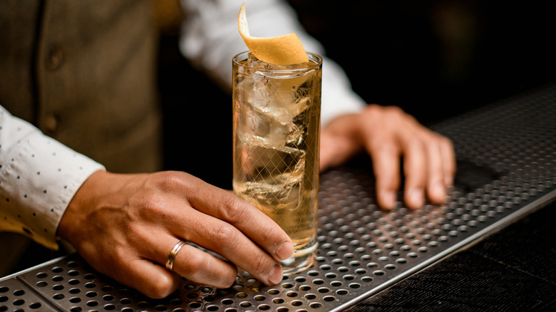 bartender's hand holding a golden colored highball with grapefruit garnish