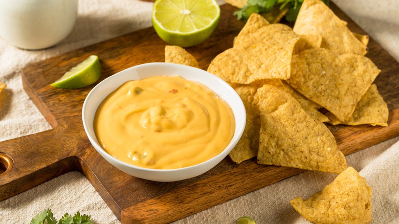 Tortilla chips next to yellow cheese sauce on a wooden board