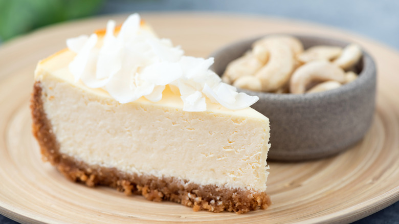 Vegan cashew cheesecake with coconut flakes served on a bamboo plate