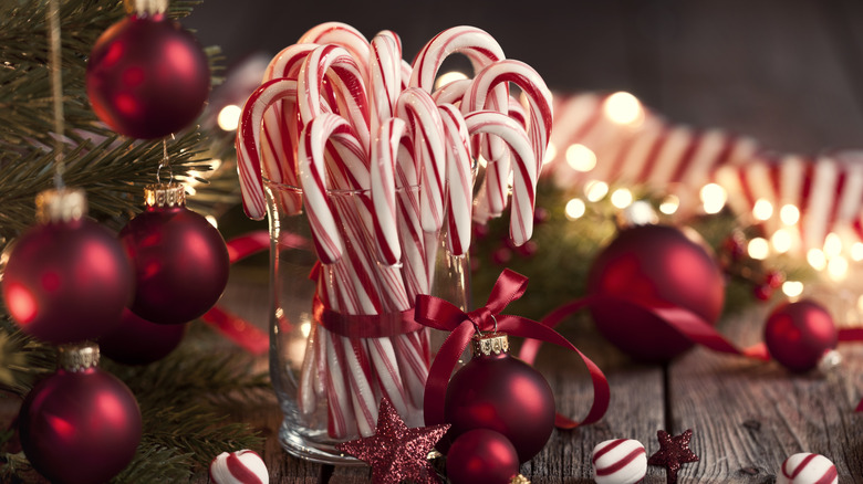 Candy canes in a glass jar surrounded by Christmas ornaments