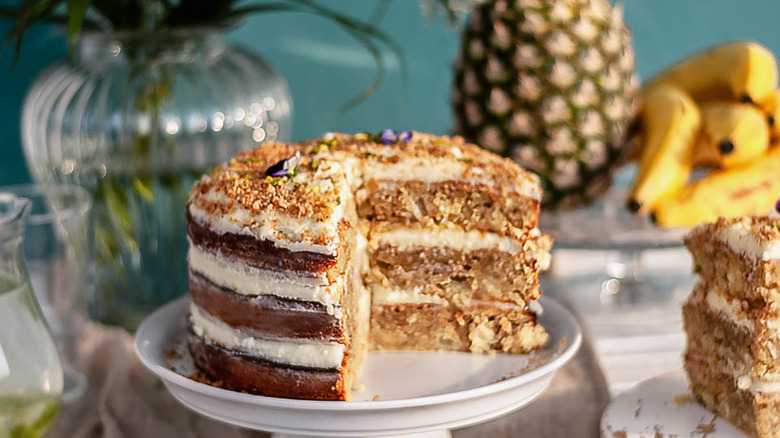 Hummingbird cake on a stand with bananas and a pineapple in the background