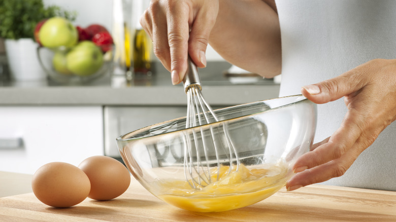 Person using balloon whisk to mix eggs