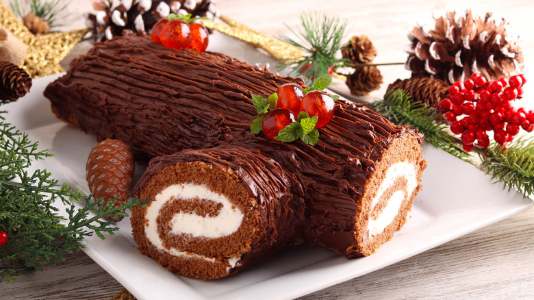 A christmas yule log cake has been cut open to reveal a swirl of cream filling inside a chocolate cake