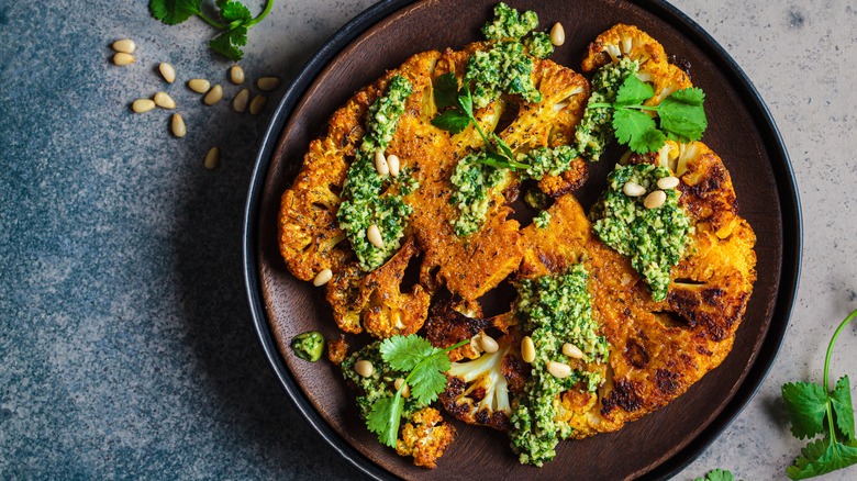 Breaded cauliflower steaks with green pesto and cilantro on black plate