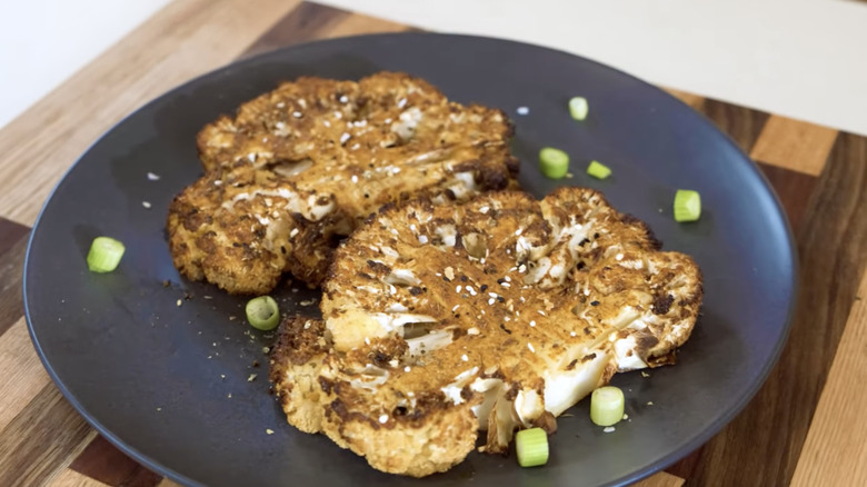 Two roasted cauliflower steaks on parchment paper baking sheet