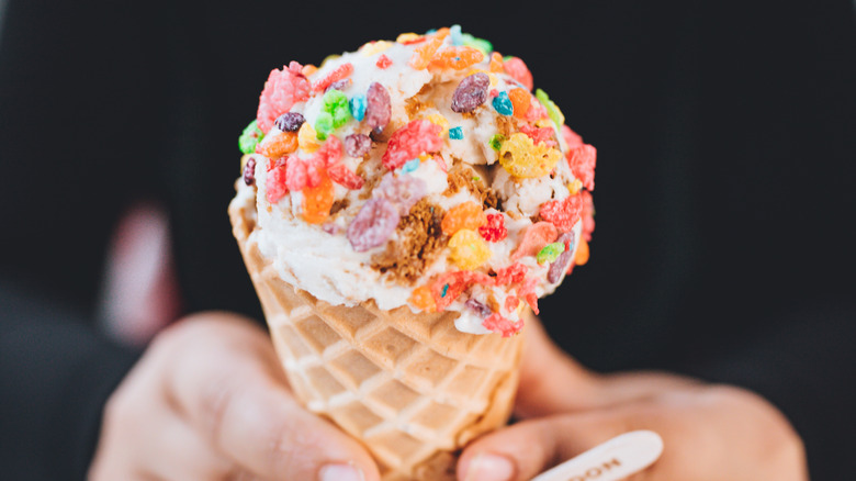 Ice cream is topped with breakfast cereal in a waffle cone.