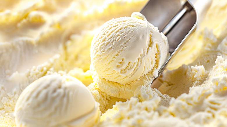 Vanilla ice cream is being scooped into balls with a metal ice cream scoop.