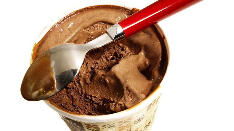 A pint of chocolate ice cream has a red-handled spoon resting upside down on top.