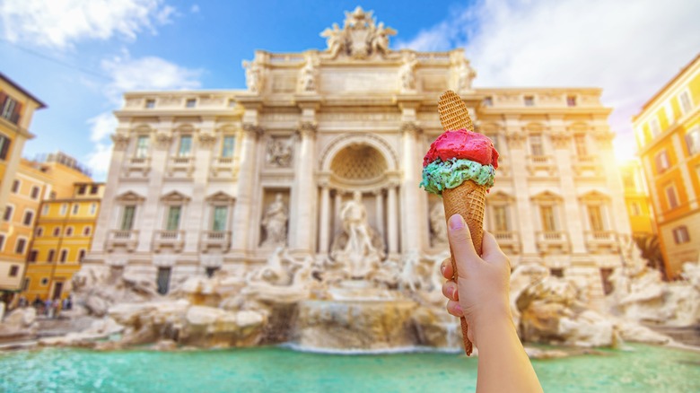 Hand holds gelato in front of Trevi Fountain