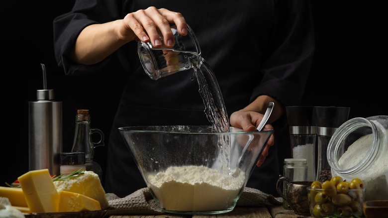 chef pouring water into bowl of flour