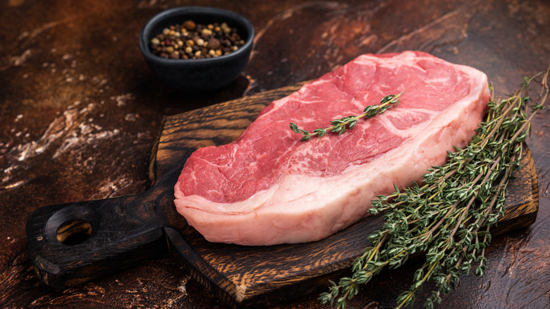 A New York strip next to fresh thyme and peppercorns