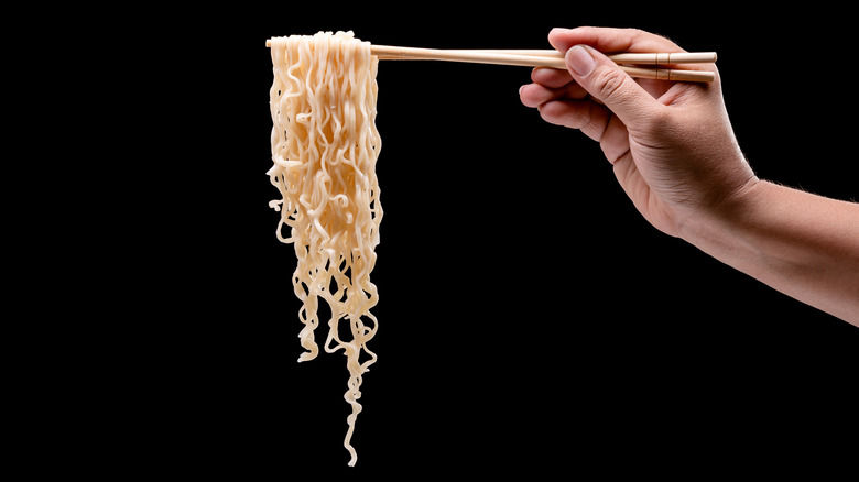 Hand holding chopsticks with noodles