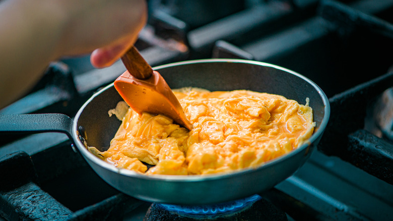 scrambling eggs in frying pan with rubber spatula 