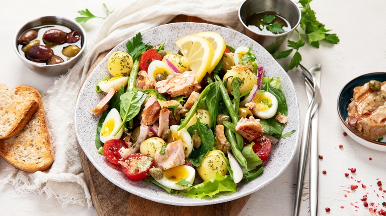 Dish of tuna nicoise salad accompanied by bread, olives, oil, and canned tuna 