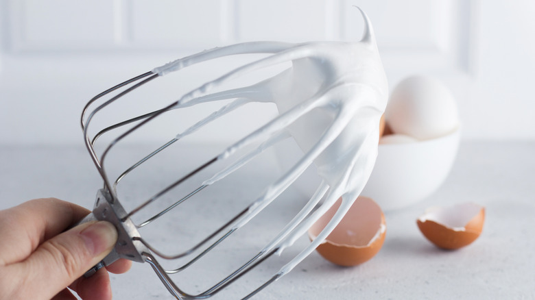 Egg whites whipped to stiff peaks clinging to a mixer whisk attachment.