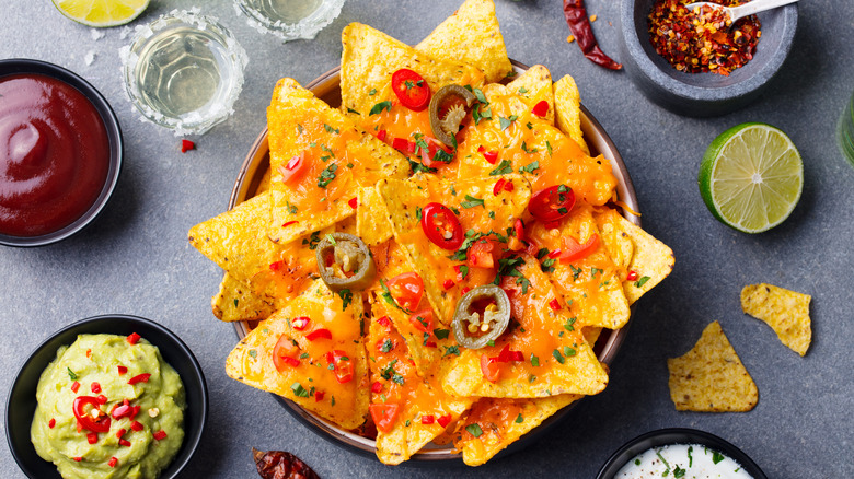 Cheese nachos in a bowl surrounded by sides of other toppings 