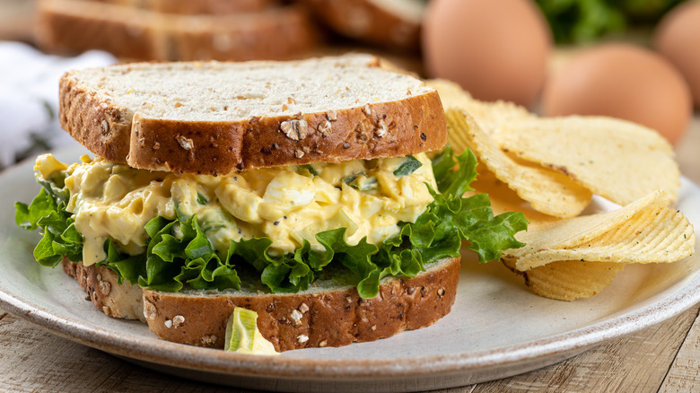 Egg salad sandwich on a plate with potato chips.