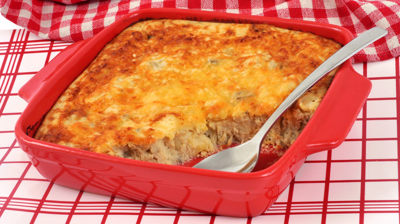 Baked brandade in a red casserole with a serving spoon