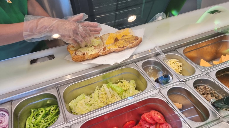 Staff member at Subway builds a sandwich from ingredients on display