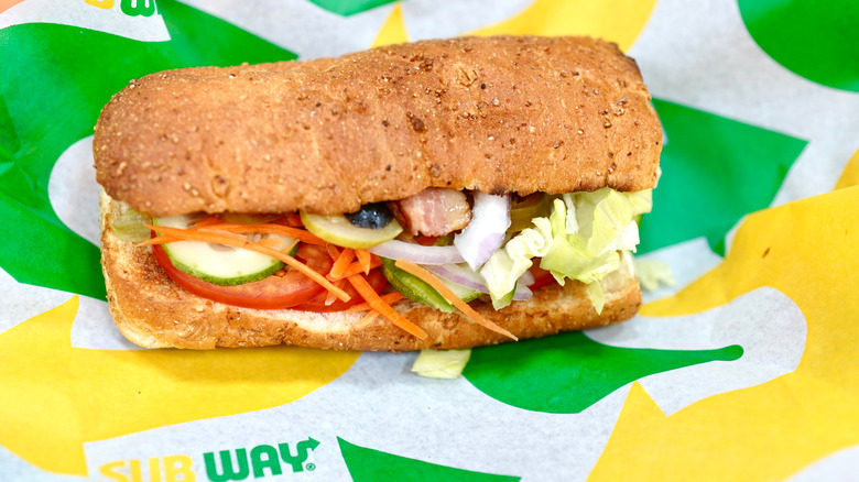 Six-inch sandwich with meat and vegetables from Subway on green and yellow paper wrapping