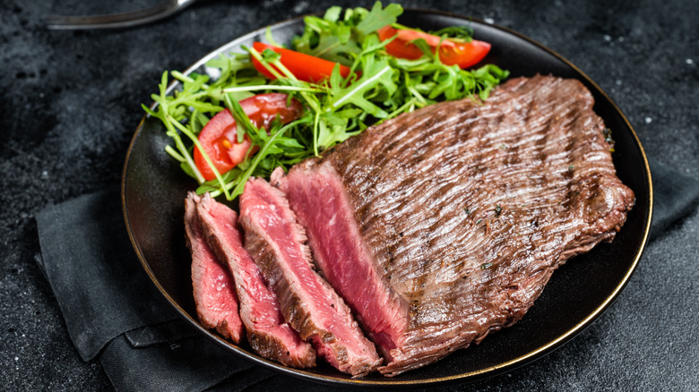 Grilled flank steak on black plate with salad