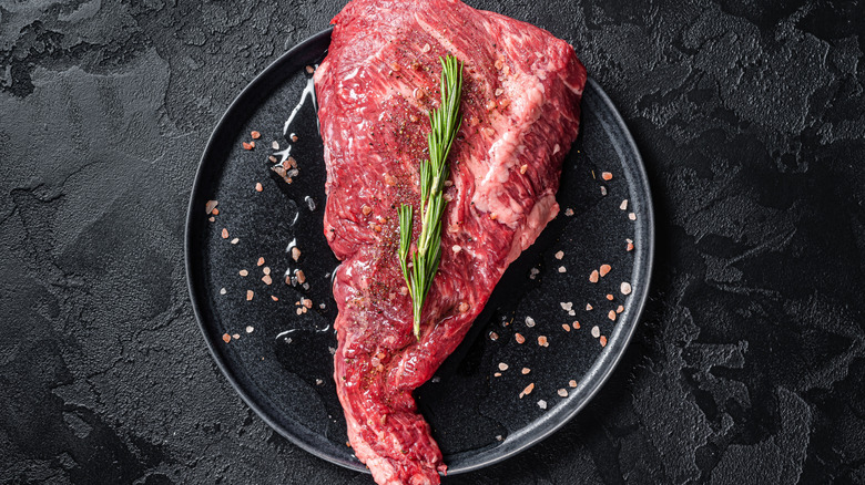 Raw Tri-tip steak with pink salt and rosemary on black plate