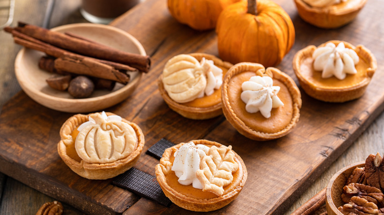 A group of mini pumpkin pies sit on a wooden surface.