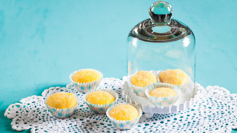 Individually wrapped yema candies rest on a lace doily with a glass cake dome