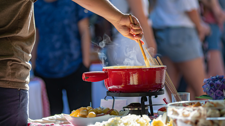 Hand stirring a fondue pot on picnic table