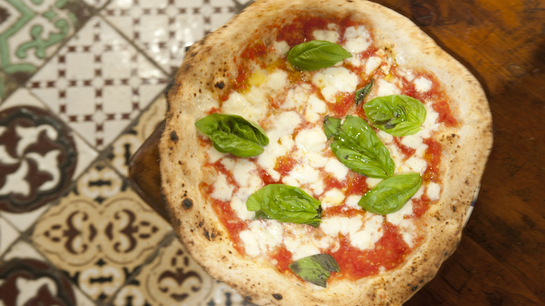 An authentic Italian pizza is displayed on a wooden table in an eatery with patterned tiled floor.