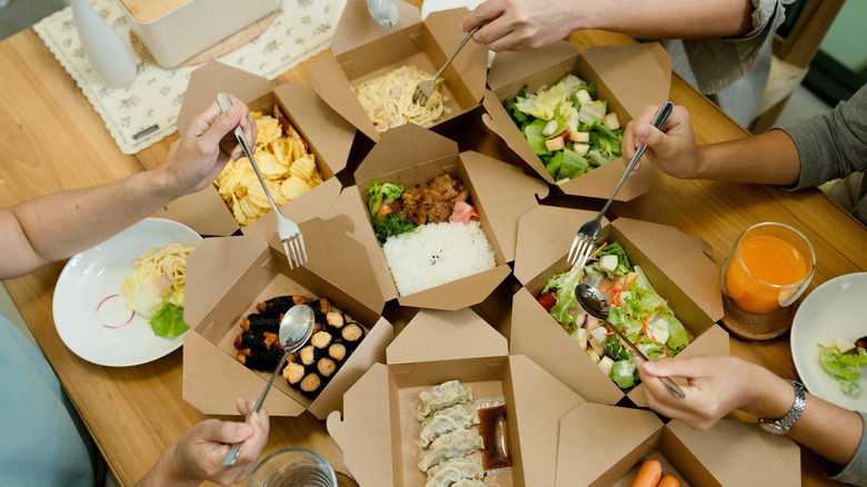 People seated at table eating food from take-out containers 