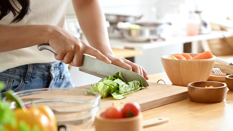 Cook chopping lettuce on wooden cutting board with knife with bowls of ingredients on the side