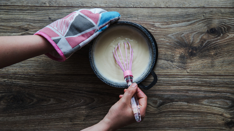 Béchamel stirred with a pink whisk in a black pot on a wooden table