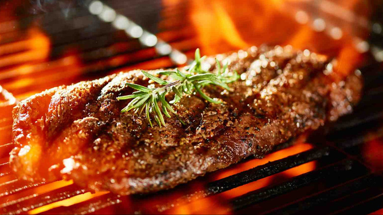 Steak cooking on a fire grill with one green rosemary sprig on top