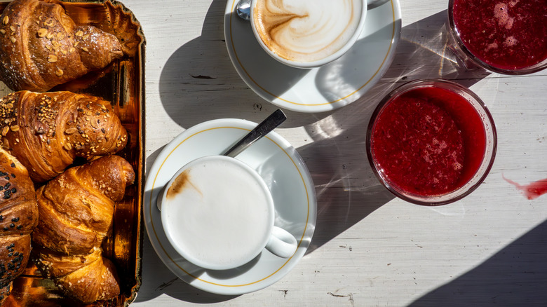 An Italian breakfast spread of cornetti and capuccinos sit on a white wooden table