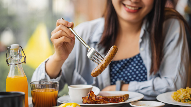 A woman spearing a link of breakfast sausage from her plate