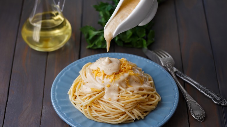 Alfredo sauce being poured over spaghetti