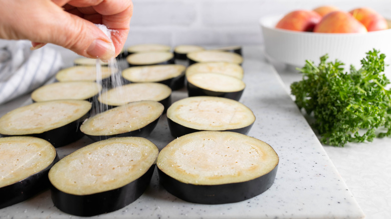 Hand sprinkling salt over slices of eggplant in kitchen