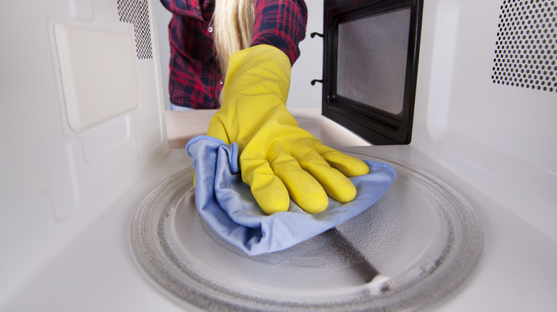 gloved hand wiping microwave turntable clean