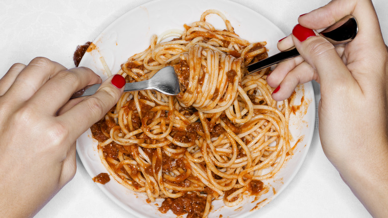 two hands with painted nails twirling spaghetti with two utensils