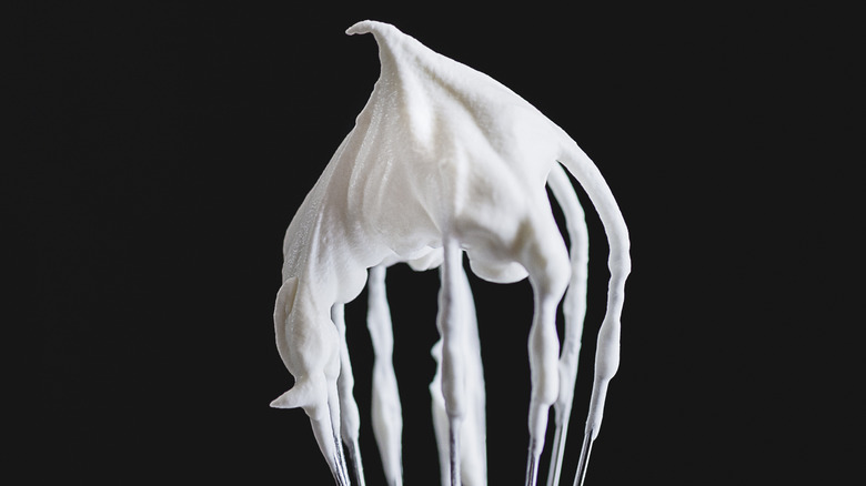 A wire whisk with whipped cream.