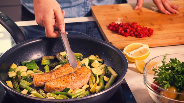 Person cooking salmon and veggies on non-stick pan