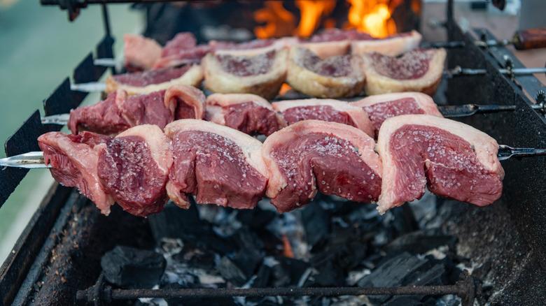 Several picanha steaks skewered on a grill over smoldering charcoal briquettes