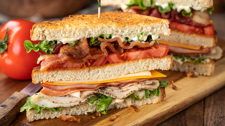 Club sandwich with three slices of triangular toast, bacon, ham, turkey, tomato, cheese