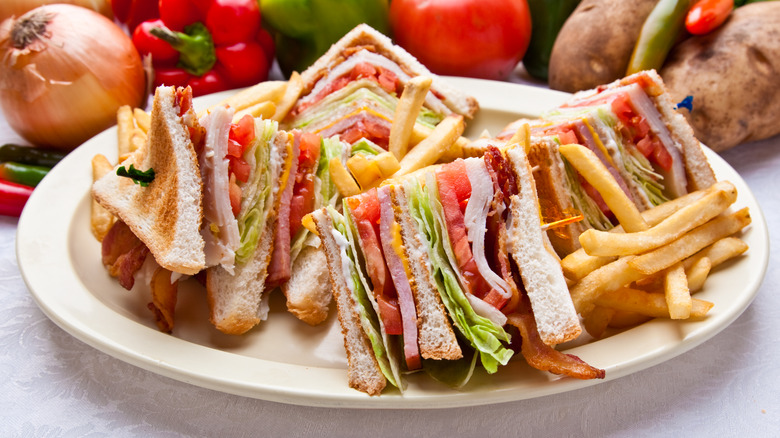 Layered club sandwich cut into four triangles on white plate with french fries