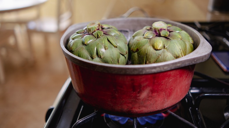 Artichokes steaming in a red pot on the stove