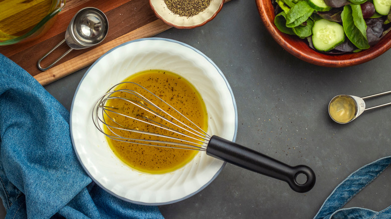 Vinaigrette in bowl with whisk and salad ingredients